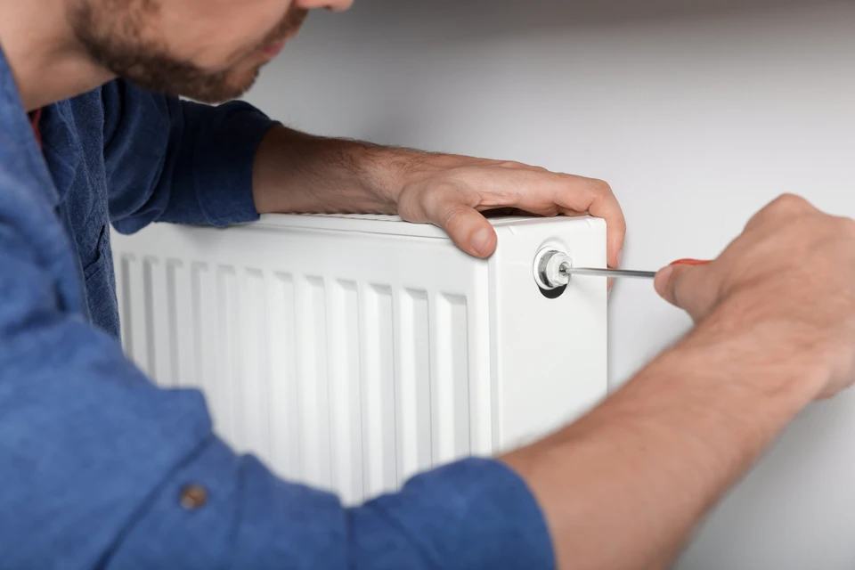 Technicien en combinaison bleue installant un radiateur blanc à panneaux dans un intérieur résidentiel