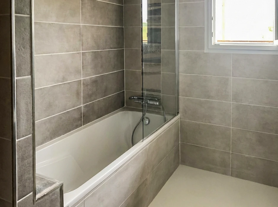 Salle de bain moderne avec baignoire encastrée blanche, paroi de douche en verre trempé, robinetterie thermostatique chromée avec douchette flexible