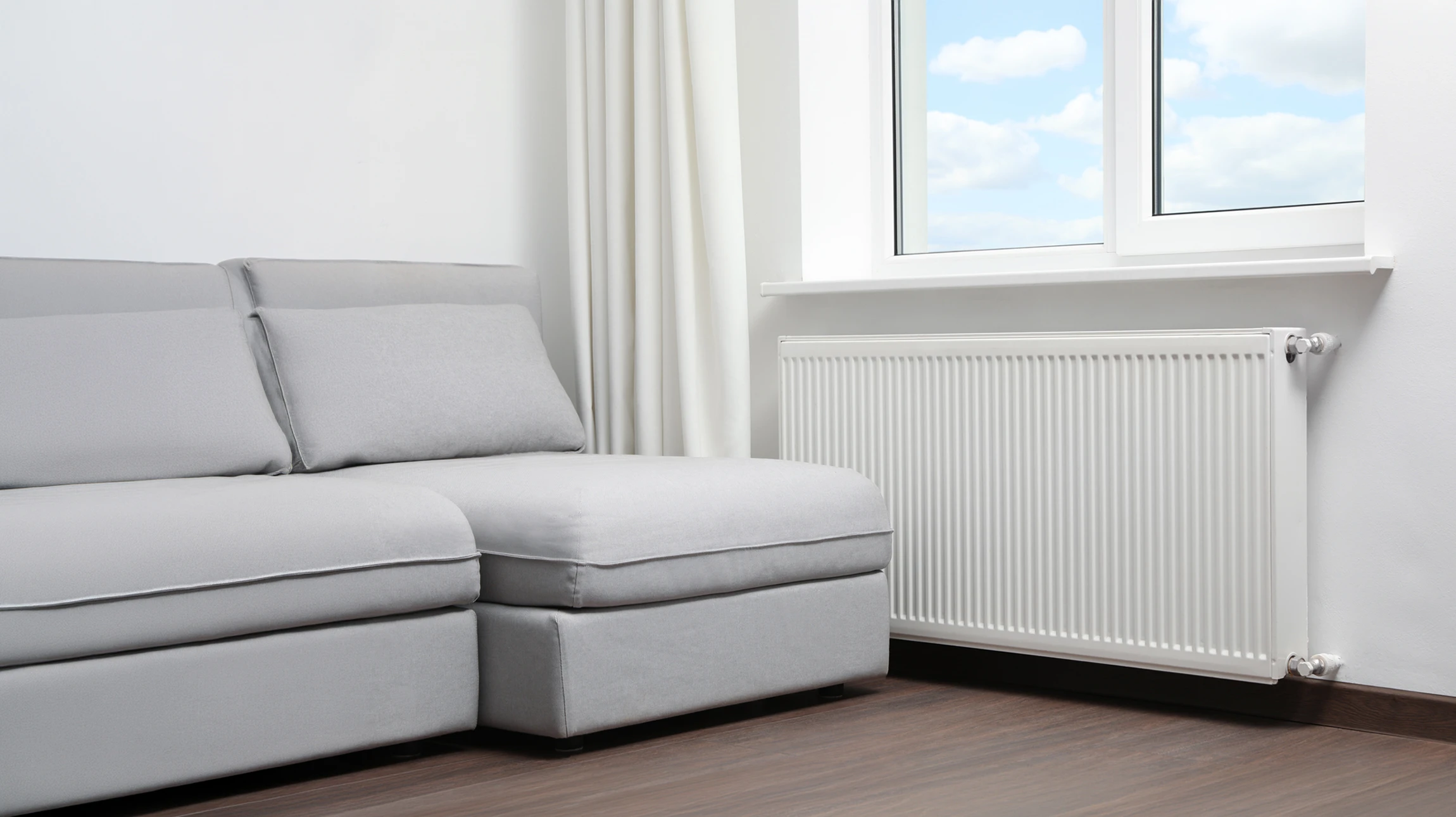 Un technicien en combinaison noire équipé d'une ceinture à outils jaune vérifie le fonctionnement d'un radiateur blanc à panneaux dans un intérieur moderne