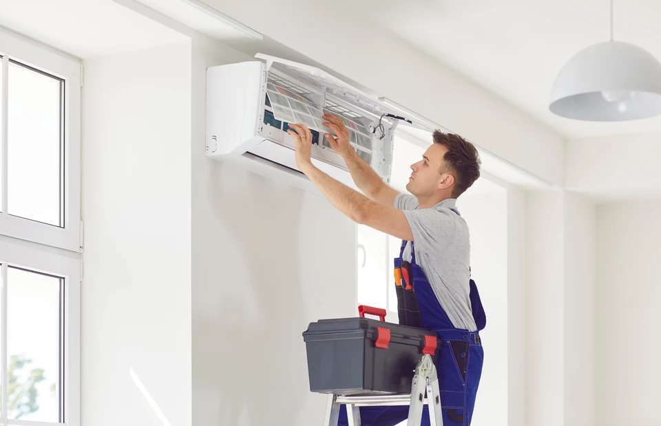 Technicien en climatisation effectuant la maintenance d'une unité de climatisation murale dans un intérieur moderne